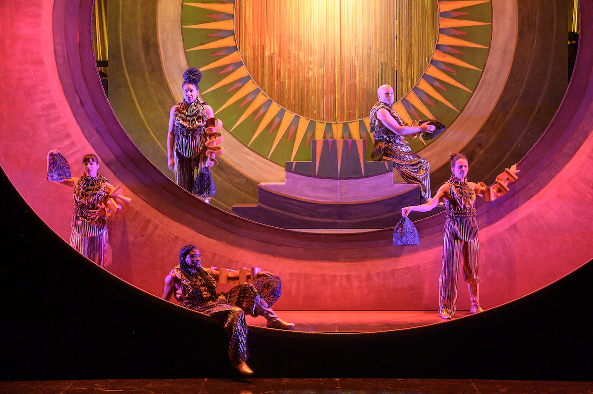 Four actors inside a giant cosmic-looking wheel.